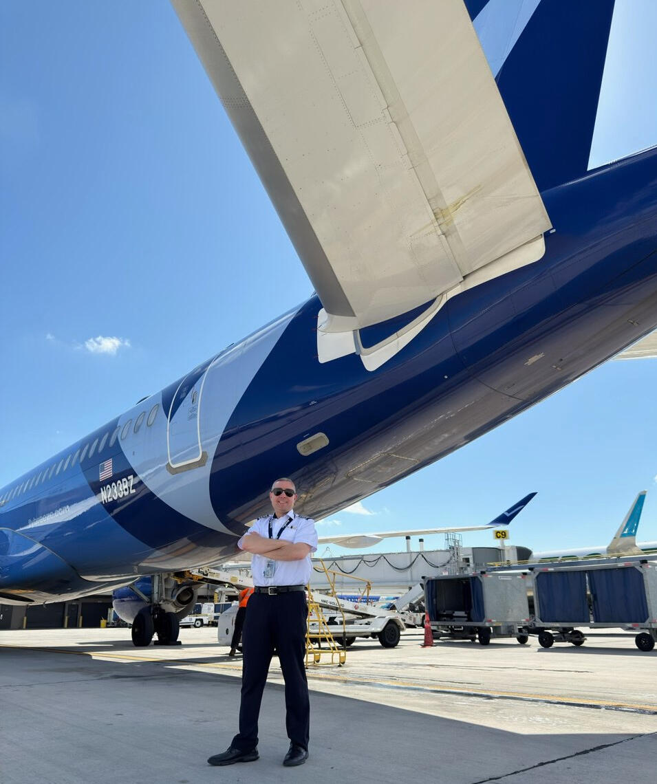 Hunter Satterwhite in captain's uniform standing beneath an airliner